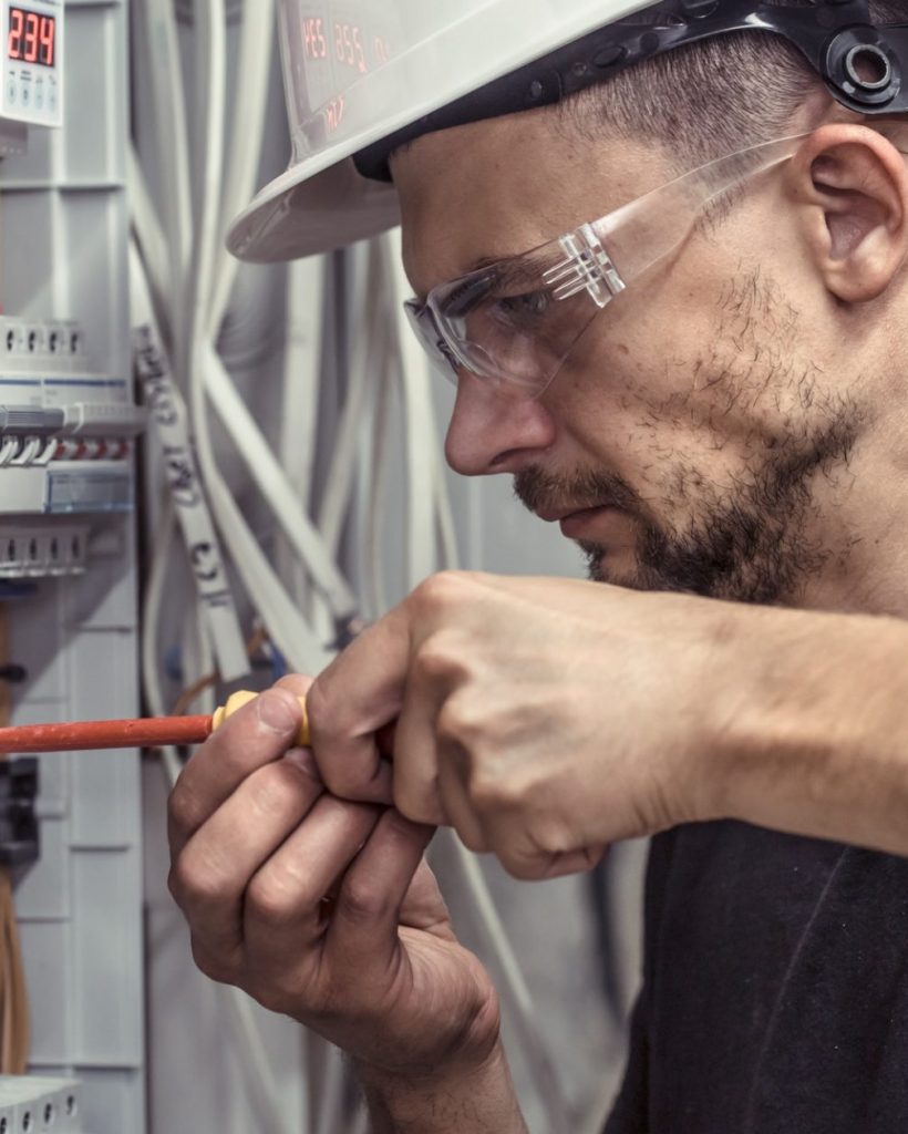 A male electrician works in a switchboard with an electrical connecting cable